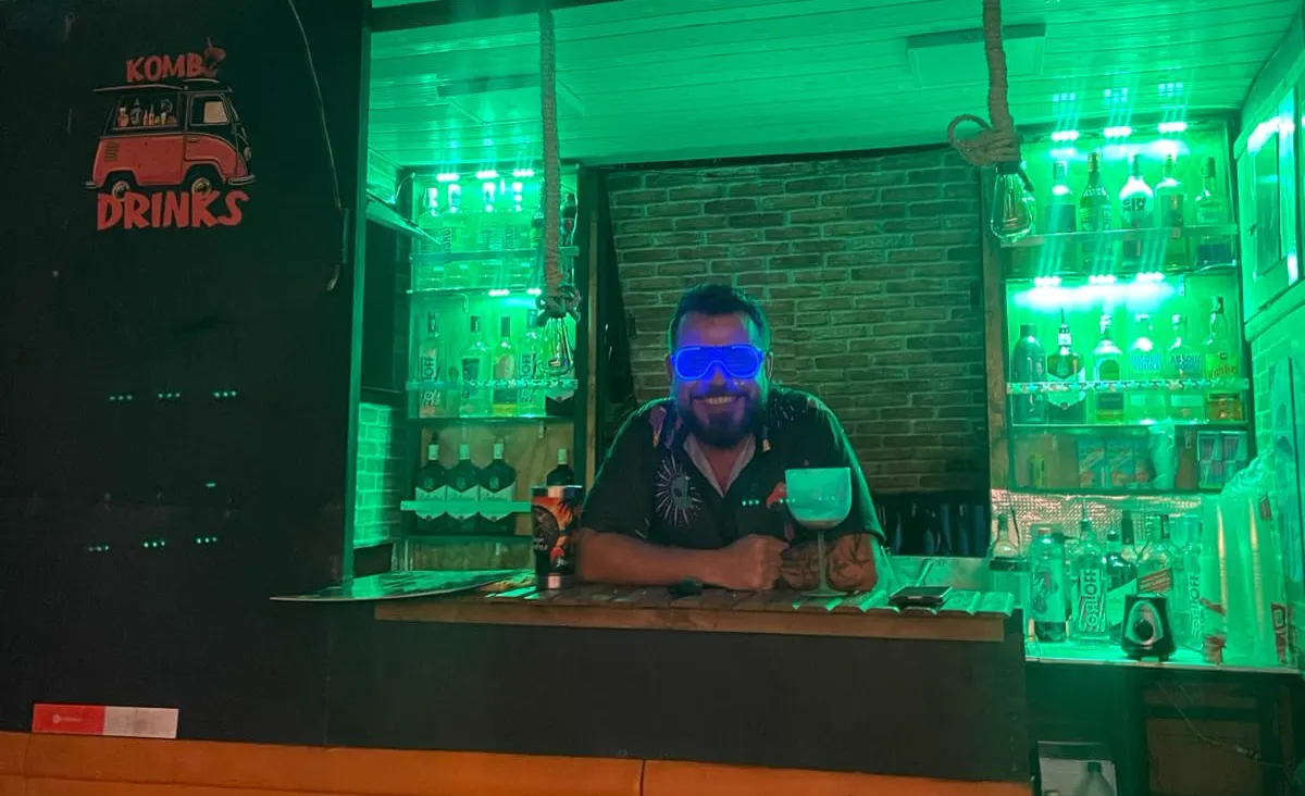 Balcão da Kombi Drinks iluminado de verde, com o bartender de óculos de LED