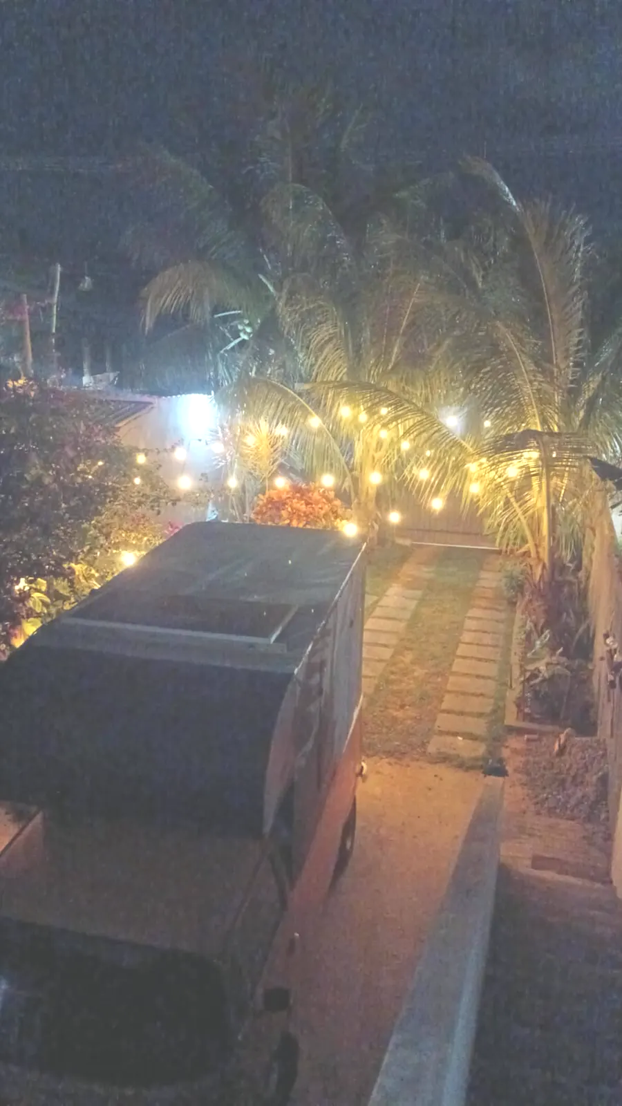 Entrada da casa vista de cima, com coqueiros e luzes