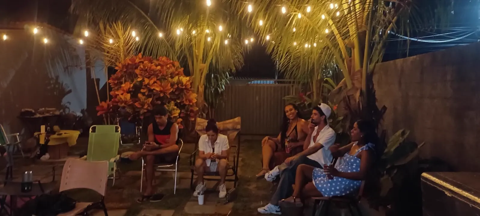 Quintal da Fazendinha à noite, com coqueiros, varal de luzes e o pessoal reunido